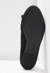 Semelle noire d'une chaussure plate New Look, taille 4/37, fabriquée en Chine, positionnée verticalement contre des surfaces blanches.