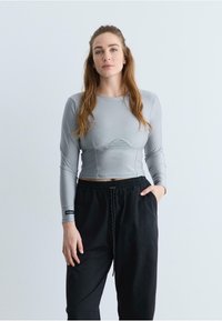 Grijze lange mouwen crop top met een aansluitende pasvorm en textuurpanelen, gecombineerd met zwarte broek met een relaxte pasvorm en een elastische tailleband.