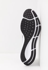 Semelle de chaussure de sport noir et blanc avec caoutchouc texturé pour une meilleure adhérence, présentant des motifs géométriques et des rainures flexibles.