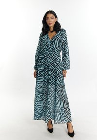 Abito lungo in leggero tessuto azzurro trasparente con strisce nere a zebra, dotato di maniche lunghe, design avvolgente e vita arricciata. Tacchi alti neri completano il look.