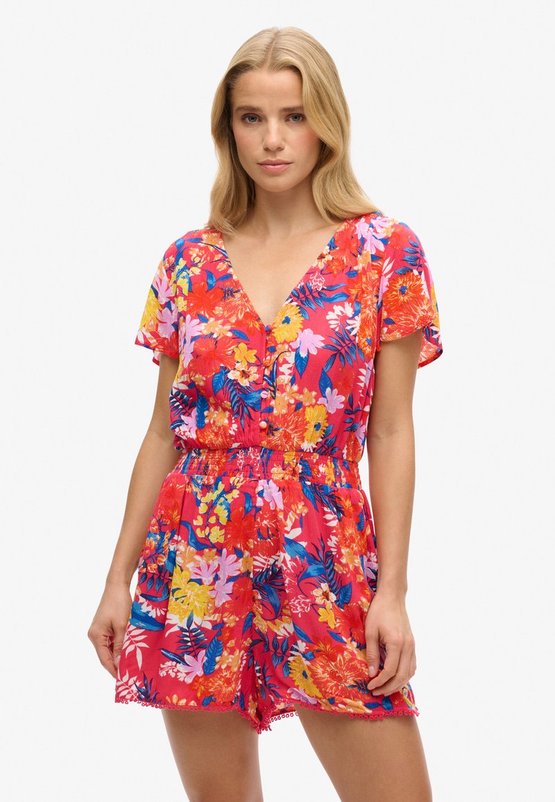 Romper floreale in un vivace rosso, con grandi fiori colorati e motivi di foglie. Maniche corte, scollo a V, vita cintrata e orlo testurizzato.