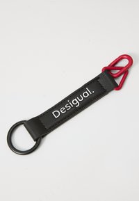 Zwarte leren sleutelhanger met een zwarte ring en een rode karabijnhaak. Heeft een reliëf "Desigual." merk op de band. Soepele structuur.