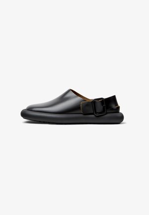 Black leather slip-on shoes with a rounded toe, a contrasting brown leather lining, and a rectangular buckle strap on the heel.