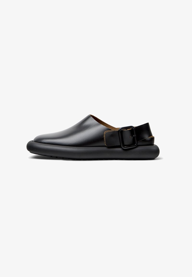 Black leather slip-on shoes with a rounded toe, a contrasting brown leather lining, and a rectangular buckle strap on the heel.
