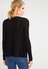 Svart textured strikkegenser med lange ermer, med et subtilt stripemønster og avslappet passform, brukt med blå denimbukser.