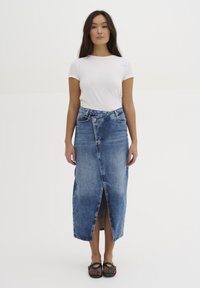 Világoskék denim maxi szoknya, elöl hasítékkal és magas derékkal. Egyszerű fehér pólóval és fekete cipővel párosítva.