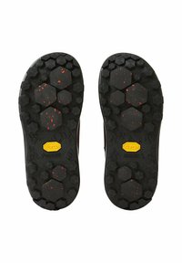 Suelas de zapatos Vibram en goma negra con patrones hexagonales y motas rojas, con un logo amarillo de Vibram para agarre y tracción.