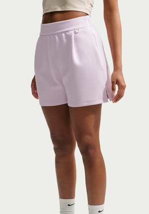 Femme portant un short violet clair avec des poches latérales et des chaussettes blanches Nike, debout devant un fond clair uni.
