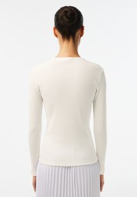 Long-sleeved, ribbed top in off-white fabric, featuring a round neckline and a fitted silhouette. Smooth texture with minimal detailing.