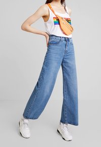 Ljusblå vida jeans med hög midja, tillverkade av denim; matchade med en vit tanktop med en färgglad grafisk design.