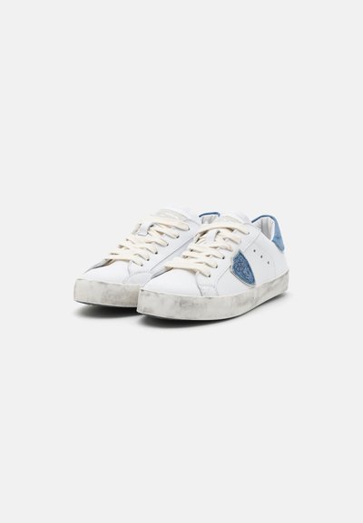 Weiße Sneakers mit blauen Akzenten, aus Leder gefertigt. Verfügen über eine strukturierte Sohle und eine abgerundete Zehenpartie. Die Schnürsenkel sind beige. Auffälliges Logo an der Seite.