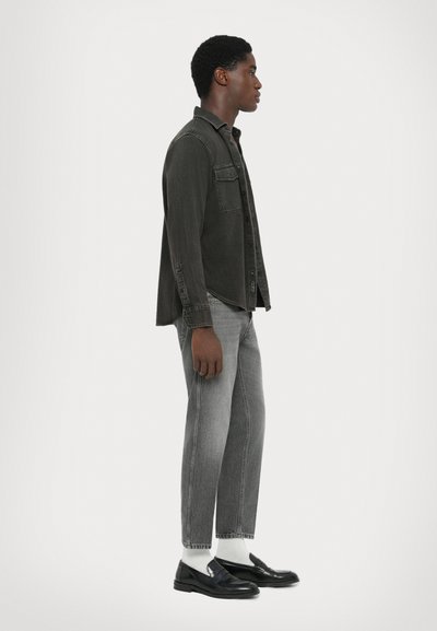 Dunkelgraues Denim-Hemd mit Kragen, einer Brusttasche und Knopfleiste, kombiniert mit grauen, taillierten Jeans und schwarzen Mokassin mit weißen Socken.