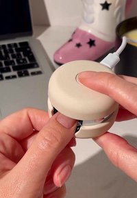 Ronde, beige siliconen apparaat met een metalen accent, vastgehouden tussen de vingers, met een zwart intern onderdeel.