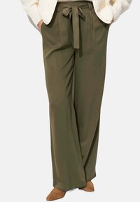 Pantalons évasés vert olive avec une texture lisse, dotés d'un détail de lien à l'avant, de plis et d'une coupe décontractée.