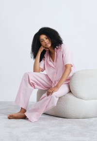 Σετ πυτζάμες ροζ ανοιχτού χρώματος με ρίγες, κοντά μανίκια και άνετο παντελόνι, κατασκευασμένο από απαλό ύφασμα. Διαθέτει κουμπιά και άνετη εφαρμογή.