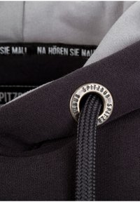 Grijze en zwarte hoodie kraag met een zilveren oogje en gevlochten trekkoord. Zachte stoftextuur met een gedeeltelijk zichtbaar label aan de binnenkant.