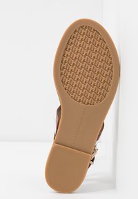 Podeszwa brązowego buta z gumowym gripem i wzorzystym bieżnikiem, na którym powtarza się logo H oraz tekst "Tommy Hilfiger".