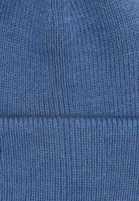 Sinine kootud beanie, millel on sooniktekstuur ja voltitud äär. Kangas tundub pehme ning kogu ulatuses on ühtlane kudumismuster.