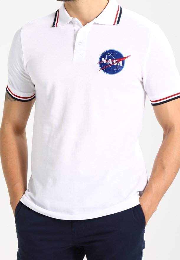 Homme portant un polo blanc avec un col et des bords de manches rayés rouges et noirs, arborant un logo de la NASA sur la poitrine.
