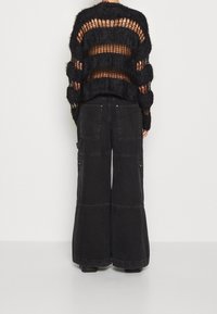 Czarny, oversize sweter dzianinowy z otwartymi paskami siateczkowymi, zestawiony z szerokimi spodniami cargo z dużymi kieszeniami i zamkami.