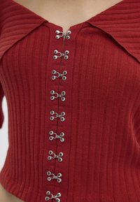 Red ribbed crop top featuring a wide collar and silver hardware detail down the center, with visible texture and a fitted shape.