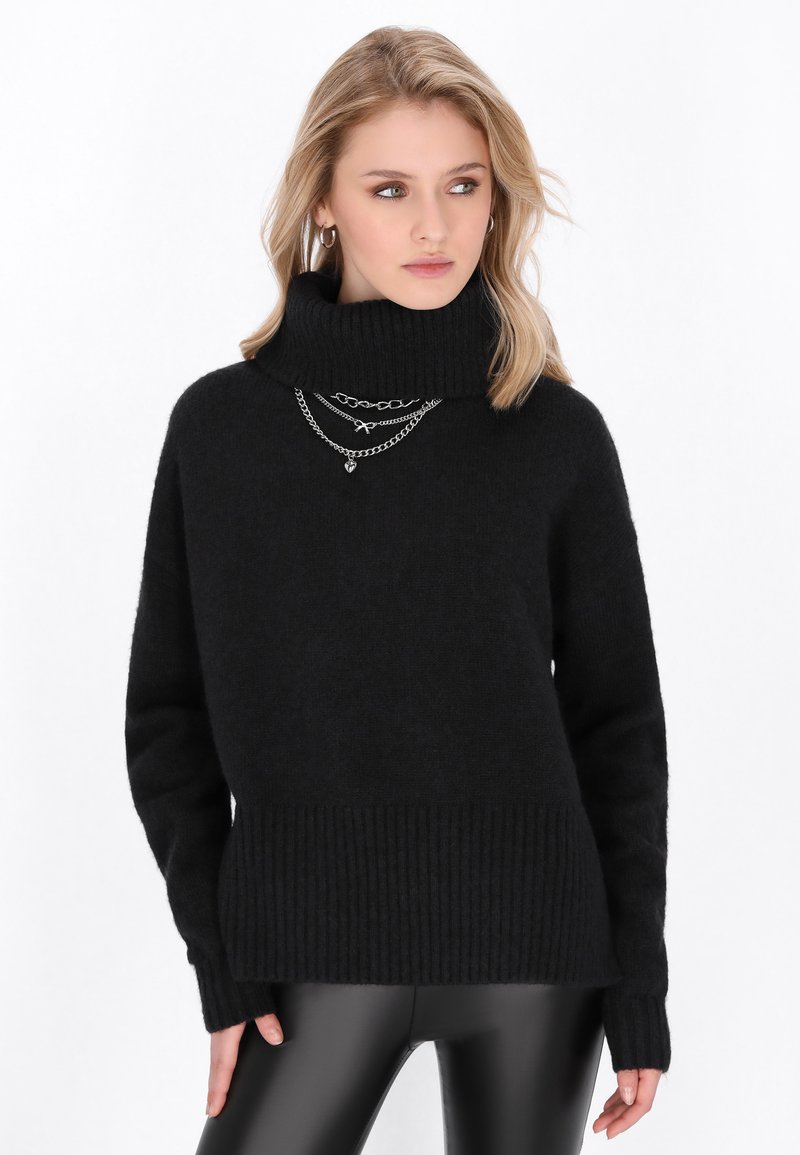 Pulover negru cu guler înalt, fabricat dintr-un material moale, texturat, cu tiv și mansete cu dungi, suprapus cu lanțuri din argint pentru detaliu.