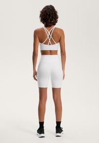 Biely športový top s krížovými ramienkami na zadnej strane, v kombinácii s bielymi šortkami s vysokým pásom, s hladkou textúrou a priliehavým strihom.