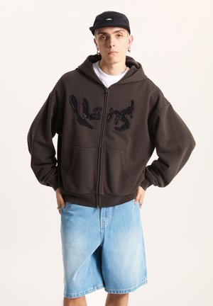 Dark brown zip-up hoodie featuring a glossy black sequin design, front pockets, and an oversized fit, paired with light blue denim shorts.