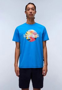 Blue cotton t-shirt with a round graphic design featuring colorful swirls and the text "NAPAPIJRI geographic" in white. Short sleeves.