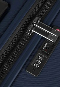 Maleta rígida azul marino en primer plano, con dos cremalleras plateadas, una cerradura de combinación con panel negro y superficie texturizada.