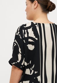 Blusa nera con motivi crema caratterizzata da maniche corte, una vestibilità rilassata, design astratti e un pannello posteriore solido crema.