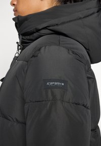 Čierna zateplená bunda s vysokou kapucňou, obsahujúca textúrovanú látku, prešívané detaily a logo Icepeak na rukáve.