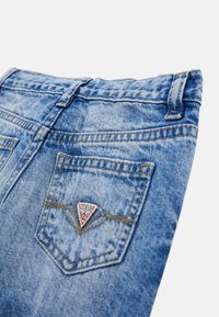 Ljusblå denimjeans med en blek textur, med en triangulär "GUESS" logopatch på bakfickan och standardbältesöglor.