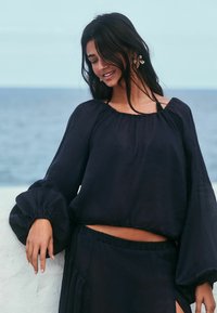 Marineblauwe, lichte blouse met pofmouwen en een losse pasvorm. Heeft een ronde halslijn en een geraffineerde taille. Gestructureerde stof.