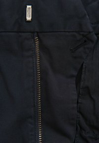 Marine stof met een diagonale textuur heeft een zilveren rits en een metalen label op de taille. De rits loopt verticaal aan de linkerkant.