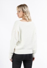 Pulover alb texturat cu o croială lejeră, cu manșete și tiv cu nervuri. Prezintă un guler larg și un material pufos, asortat cu pantaloni negri mulați.