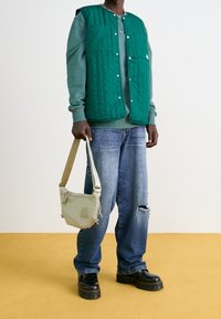 Chaleco acolchado verde sobre un sudadera verde, combinado con unos jeans azules holgados con rotos. Accesorio es un bolso cruzado beige. Botas negras de plataforma.