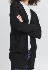 Mustat kardiganit, jotka on valmistettu pehmeästä materiaalista, löysällä istuvuudella, avonaisella edellä ja kahdella etutaskulla. Niissä on pitkät hihat ja ribbitettu pinta.