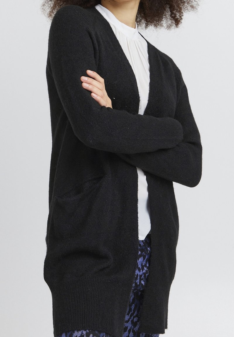 Mustat kardiganit, jotka on valmistettu pehmeästä materiaalista, löysällä istuvuudella, avonaisella edellä ja kahdella etutaskulla. Niissä on pitkät hihat ja ribbitettu pinta.