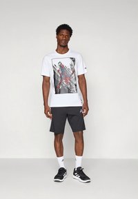 White short-sleeve t-shirt featuring a Spider-Man graphic, paired with black shorts. Accented with three white stripes on the shorts.