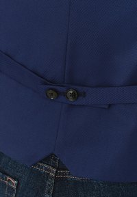 Granatowa teksturowana kurtka z wyrazistym kołnierzem, dwiema czarnymi guzikami i dopasowanym krojem, w połączeniu z ciemnymi dżinsami.