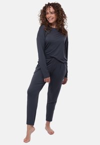 Completo da loungewear grigio antracite composto da una maglietta a maniche lunghe con vestibilità comoda e pantaloni a tasca, realizzati in tessuto morbido e liscio.