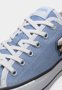 Ανοιχτό μπλε καμβά sneaker με λευκά κορδόνια, ασημένια οπές και καρτούν λογότυπο στο πλάι κοντά στη σόλα.