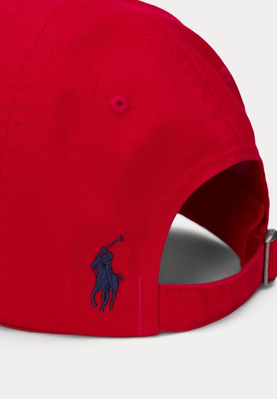 Červená bavlněná čepice s zakřiveným kšiltem, obsahující vyšívané námořnické modré logo hráče póla na levé straně a nastavitelný zadní popruh.