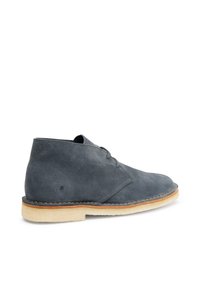 Stivali alla caviglia in suede grigio con punta rotonda, design minimal con lacci, suola beige a contrasto e dettagli cuciti lungo il bordo.