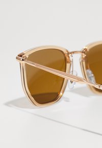 Ochelari de soare cu rame transparente de culoare roz, lentile maronii și brațe metalice elegante, cu accente texturate pe laterale.