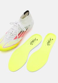 Chaussure de sport blanche avec des accents vifs en jaune et rose, présentant un col en forme de chaussette et une semelle intérieure jaune assortie exposée à côté.