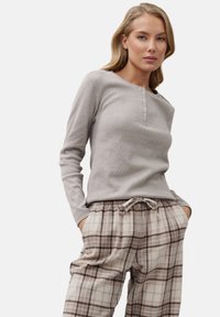 Top henley gris claro de manga larga con cuello redondo y tapeta de tres botones, combinado con pantalones de cuadros en tonos beige y marrón con cordón.