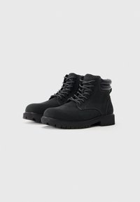 Botines negros de ante con puntera redonda, cuello acolchado, diseño con cordones y suela de goma texturizada que presenta patrones de profundidad.