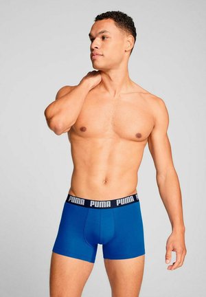 Blue boxer briefs made of stretch fabric, featuring a black waistband with white "PUMA" logo. Smooth texture and fitted design.
